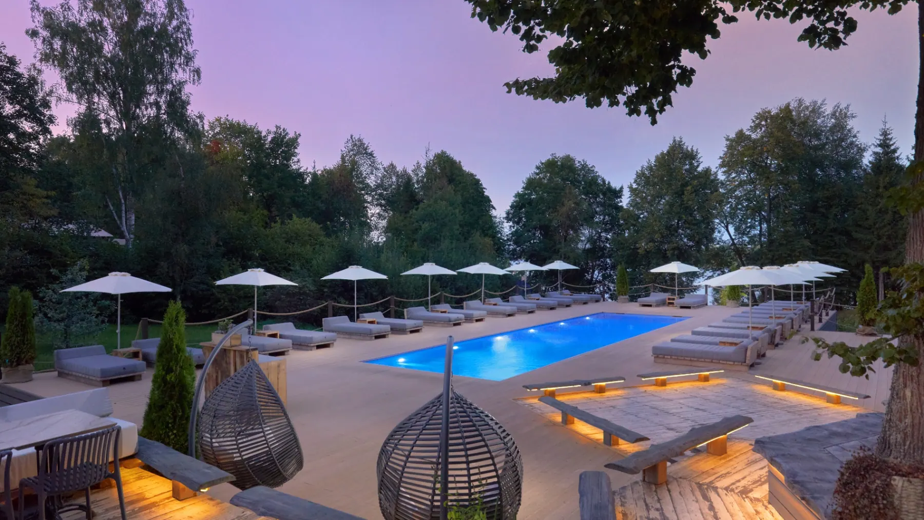 Resort pool deck at Berta Village at twilight with lounge chairs and forest views